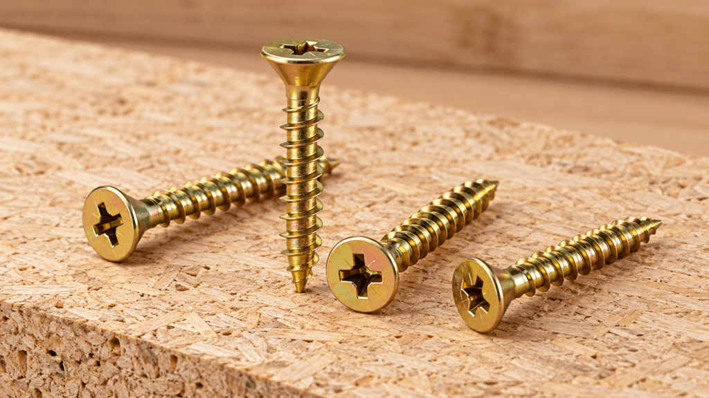 Golden chipboard screws placed on a wooden particle board surface for furniture and cabinetry use
